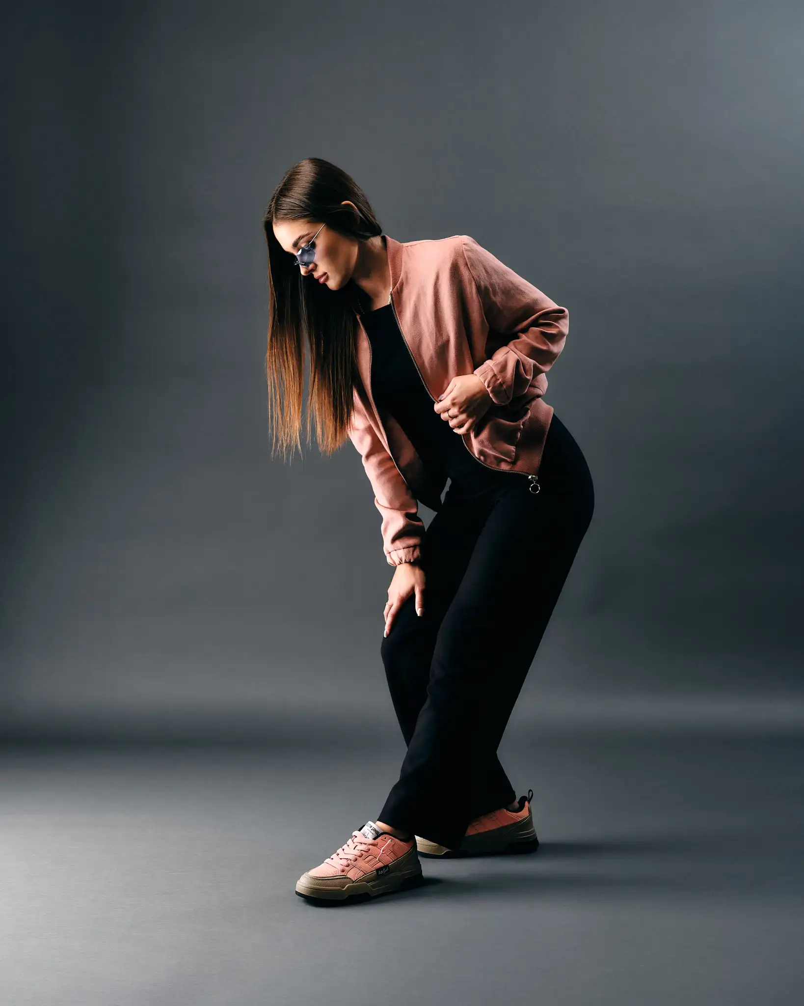 Vrouwelijk model in roze bomberjack en roze Austin Gamble sneakers poseert in studio